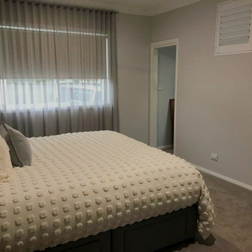 A Bedroom With a Bed , Curtains and a Window — Winning Blinds in Cardiff, NSW