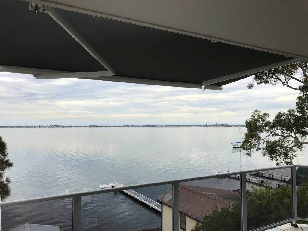 A Black and White Striped Awning is Hanging on a Brick Wall  — Winning Blinds in Cardiff, NSW