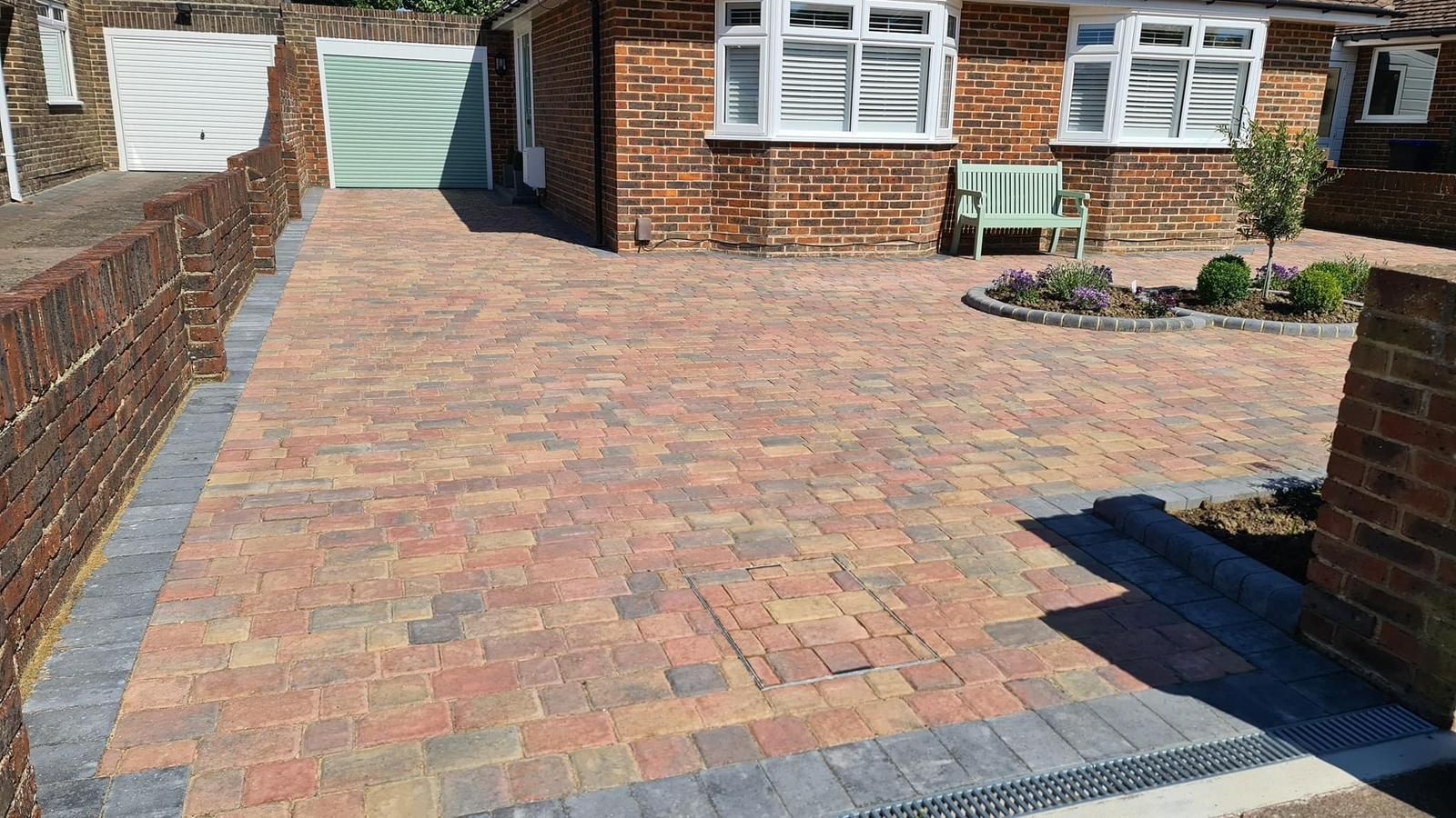 Newly installed block paving driveway in Woking outside a brick home with a small front garden and green bench.