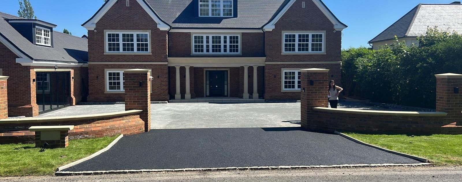 A large brick house with a paved driveway and a clear blue sky.