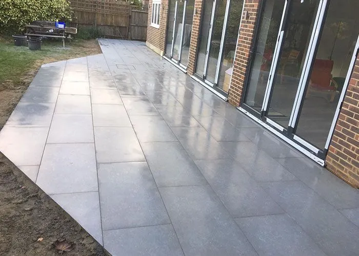 New grey patio in Woking by Surrey Hills, leading to bi-fold doors on a home.