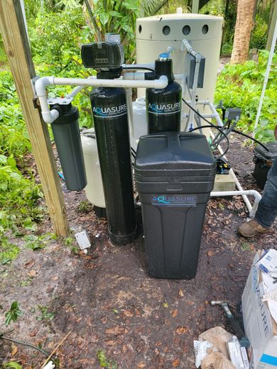 Outdoor water filtration system with tanks, a brine cabinet, and piping situated in a wooded area.