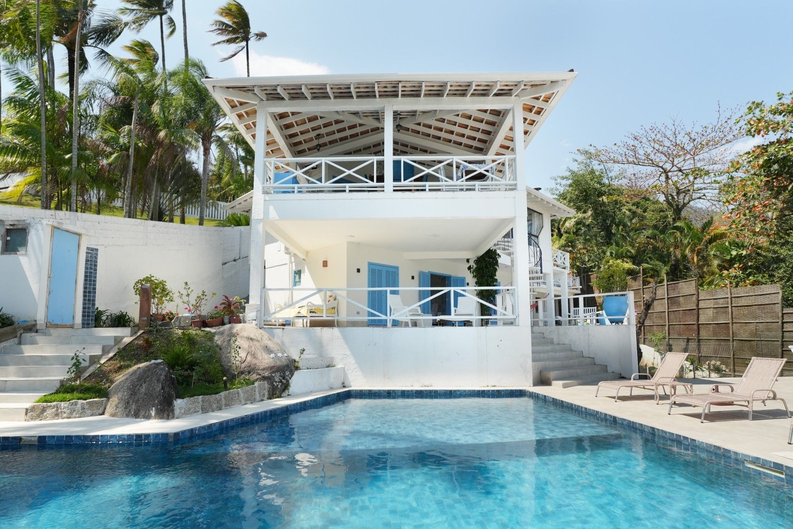 Moradia moderna branca com piscina e vista para o mar, rodeada por palmeiras e espreguiçadeiras.
