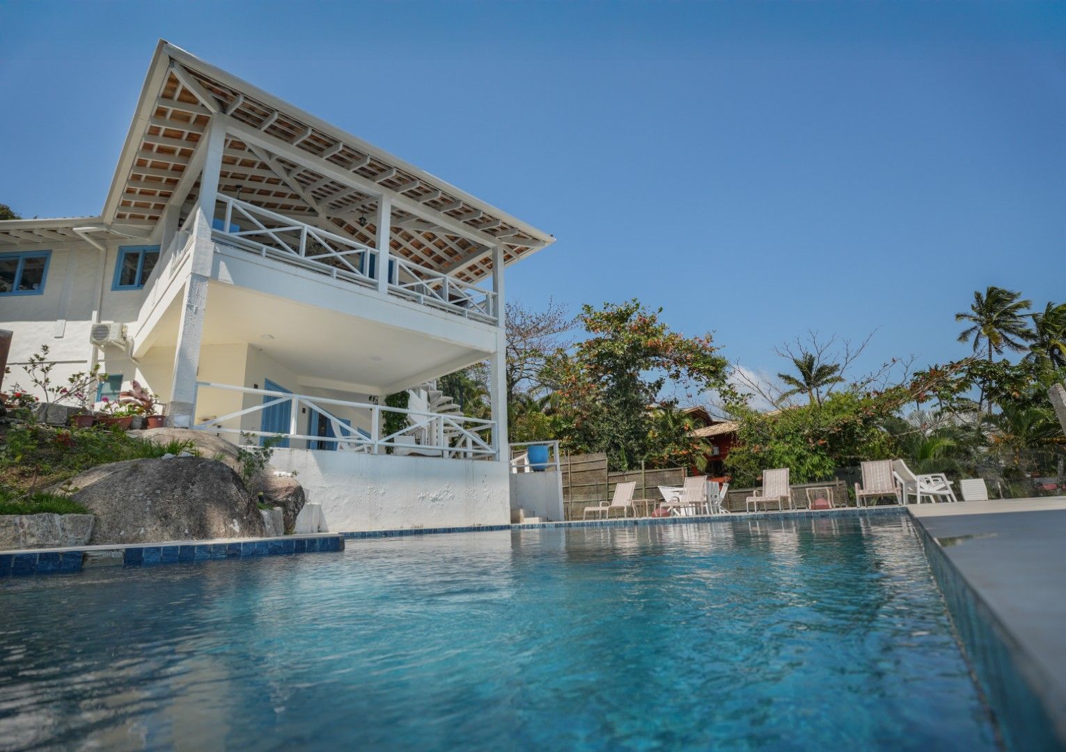 Vila branca à beira-mar com piscina sob um céu azul.