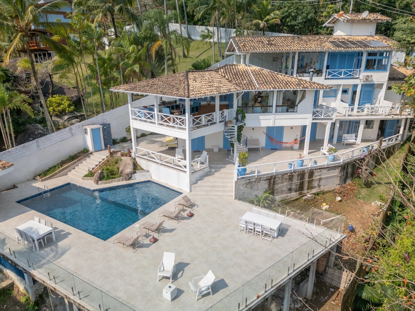 Vista aérea de uma casa branca com piscina, pátio e localização privilegiada em uma encosta à beira-mar.