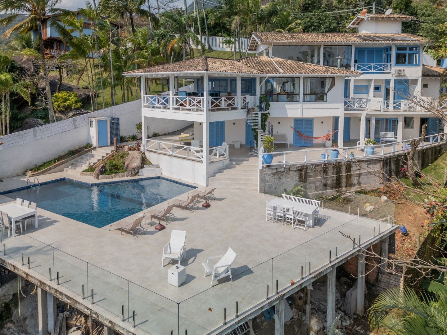 Moradia moderna branca à beira-mar com piscina e terraço na cobertura, situada numa encosta tropical.