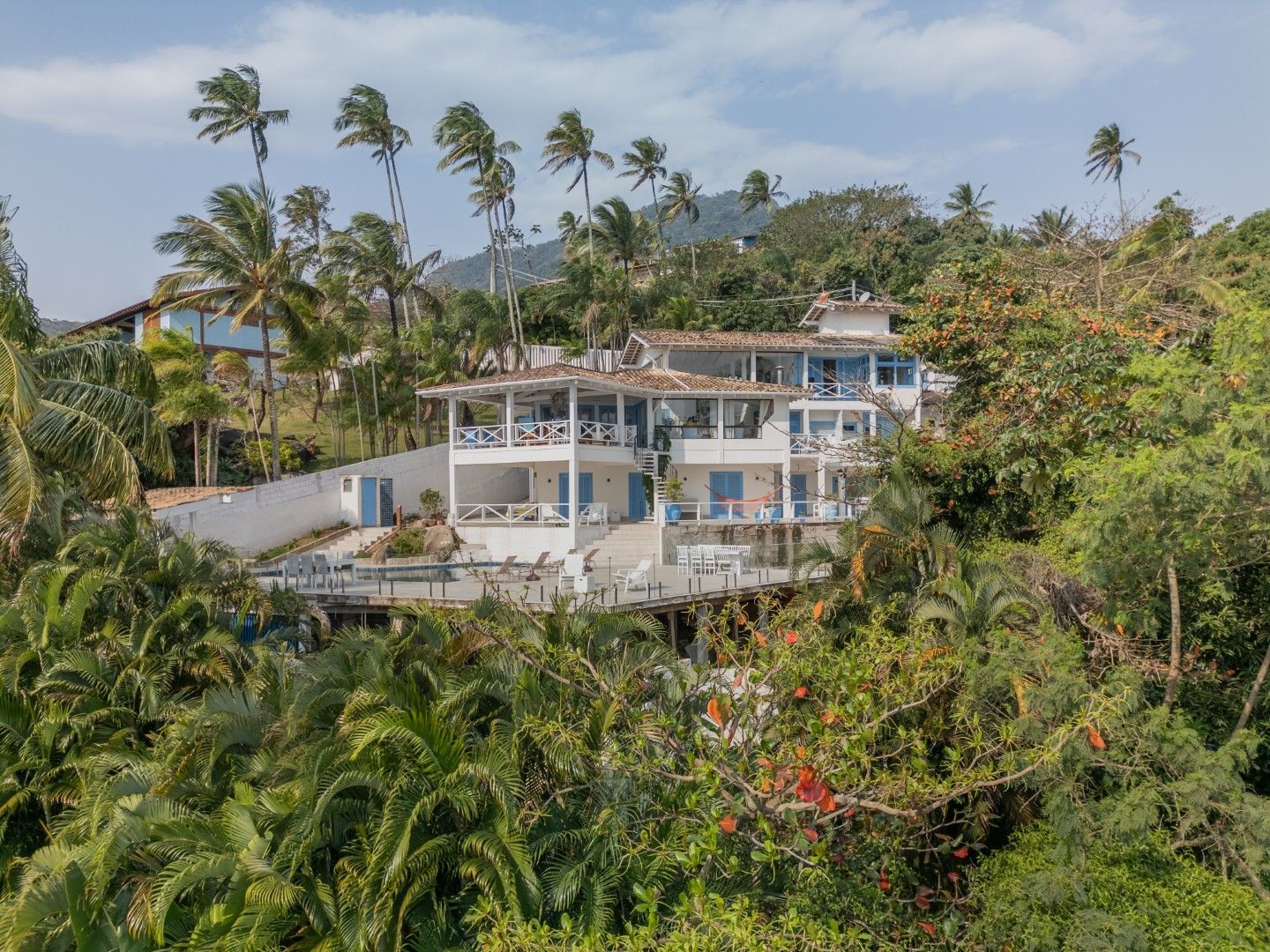 Vila branca na encosta, com palmeiras e vegetação tropical exuberante sob um céu azul.