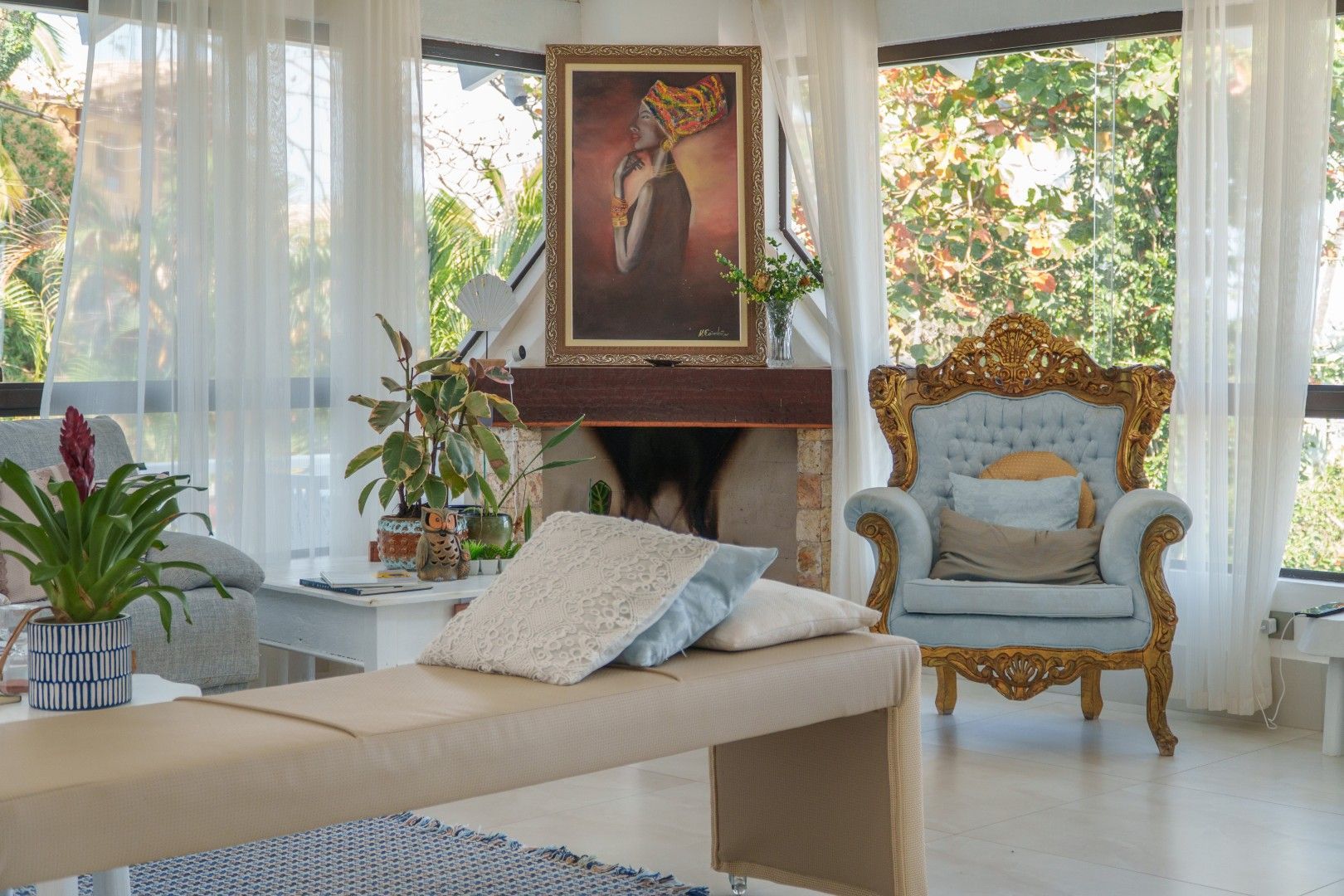 Sala de estar elegante e ensolarada com cortinas brancas, cadeira dourada ornamentada, chaise longue bege e retrato floral.