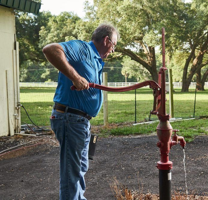 A man in a blue shirt is pumping water from a red pump