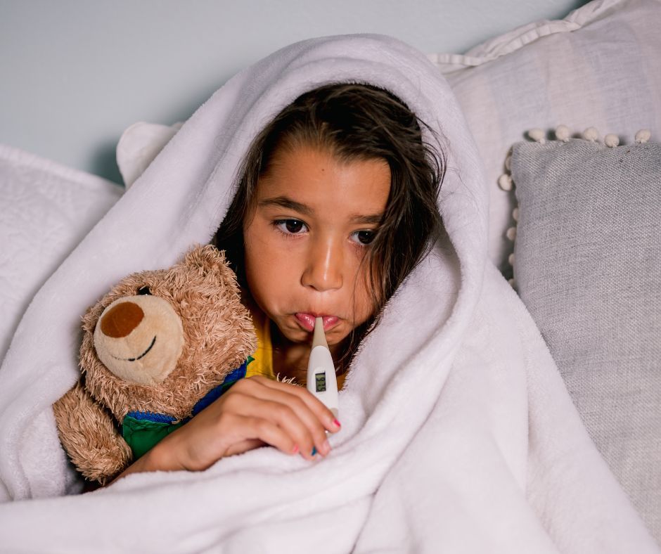 Sick child with a thermometer and teddy bear.