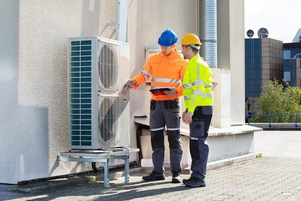 two men are standing next to each other in front of a building looking at an air conditioner .