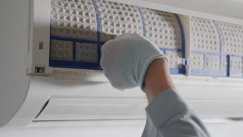 a person is cleaning an air conditioner with a pair of gloves .