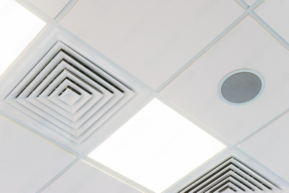 a close up of a ceiling with square vents and a speaker .