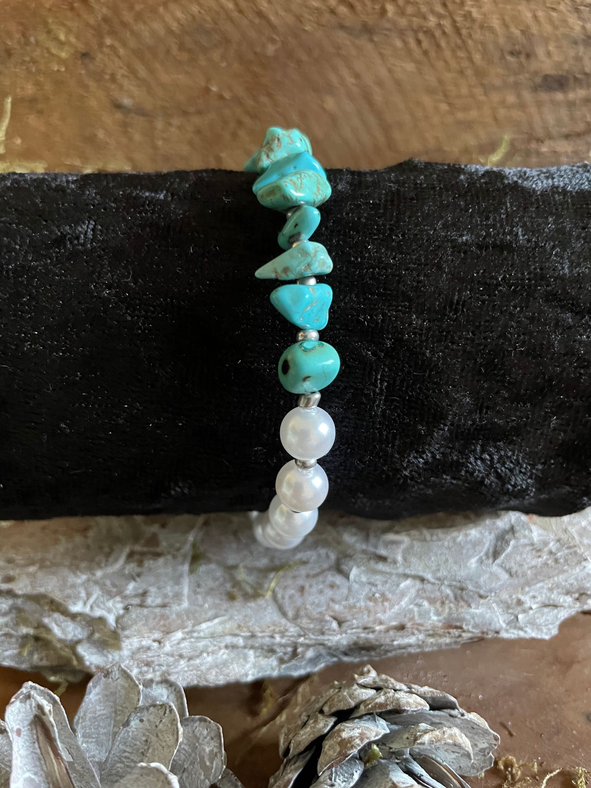 Armband met turquoise en witte kralen op een zwart-zilveren ondergrond.
