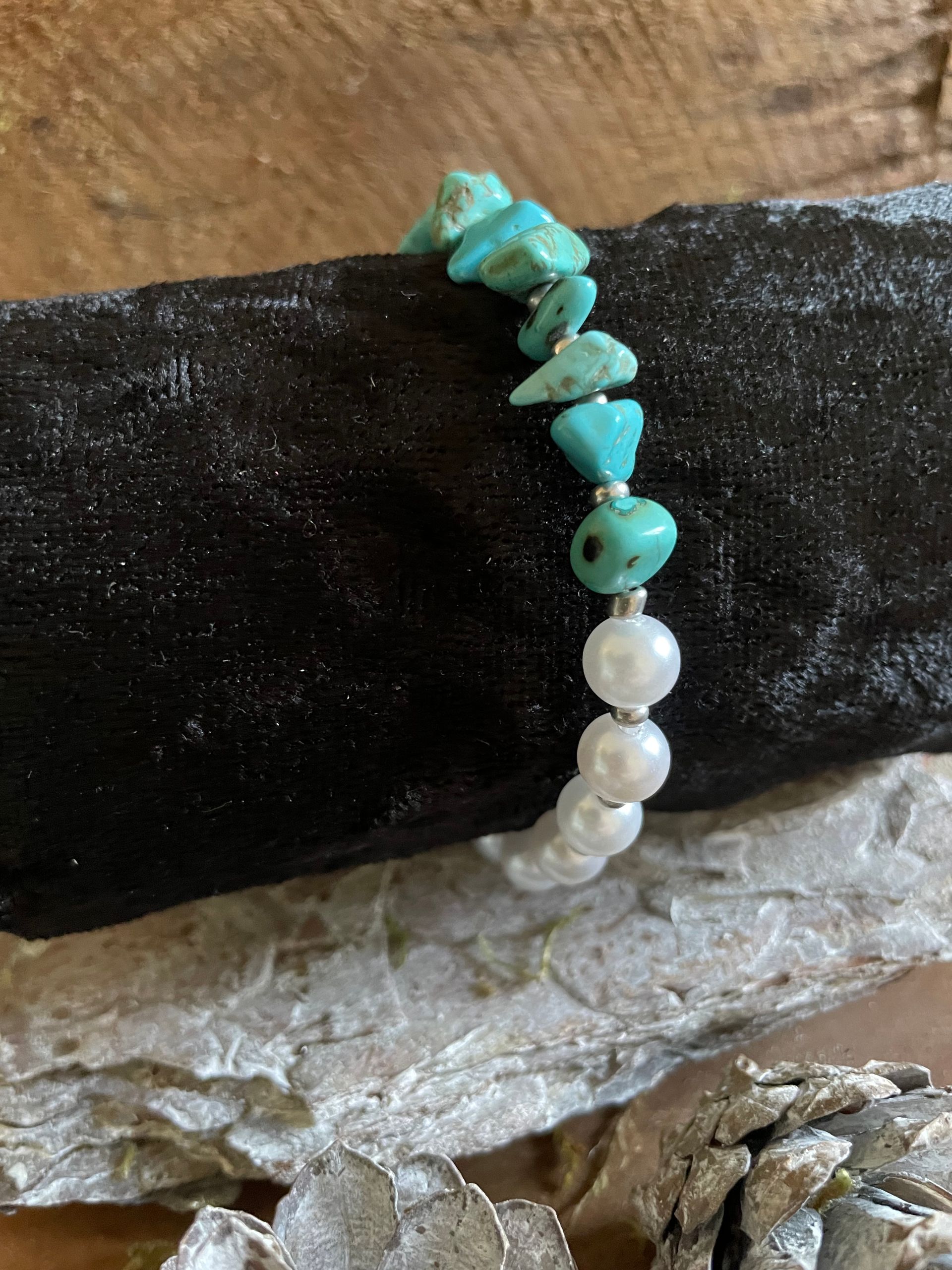 Armband met turquoise en witte kralen op een zwart-zilveren ondergrond.