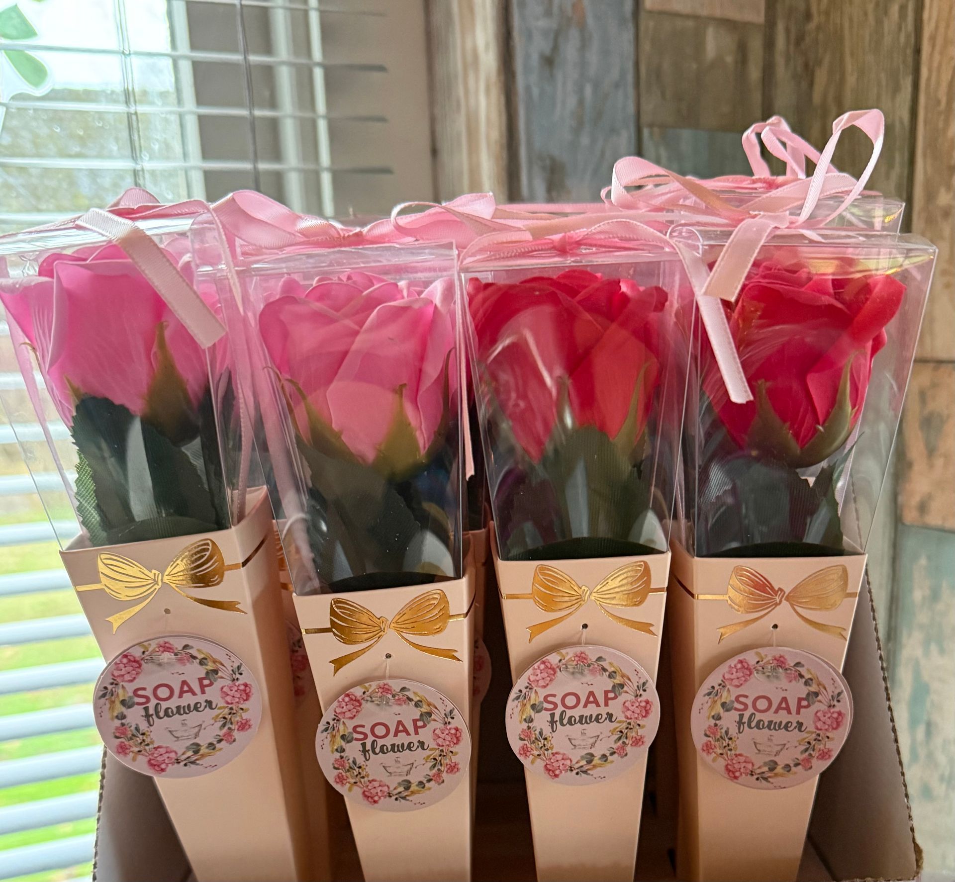Vier zeepbloemen in de vorm van rozen, verpakt in een transparante verpakking met lint en decoratieve labels.