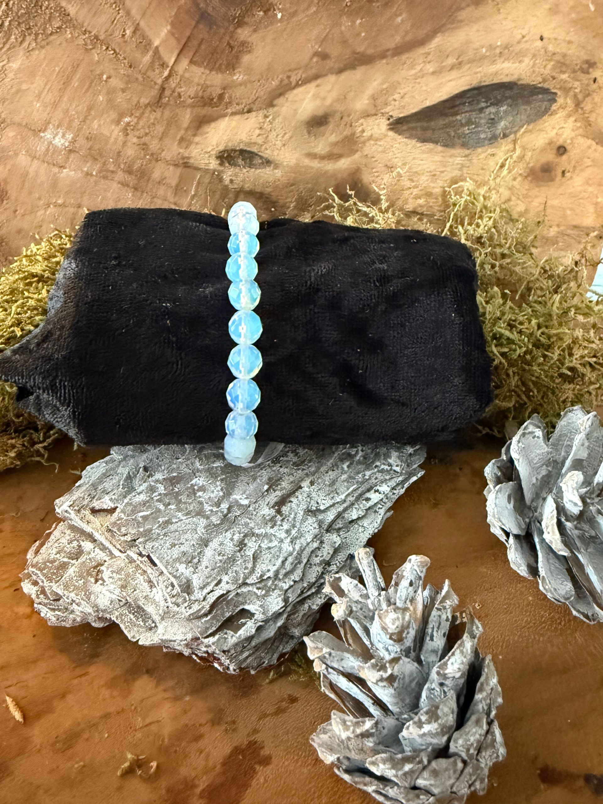 Lichtblauwe kralenarmband op een zwart, gestructureerd blok; tentoongesteld op hout, boomschors en dennenappels.