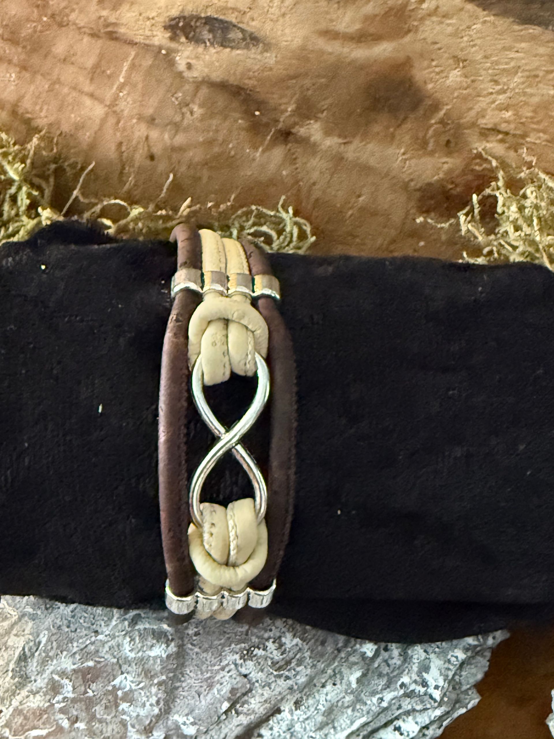 Bruine leren armband met een zilveren oneindigheidssymbool en crèmekleurige knopen.
