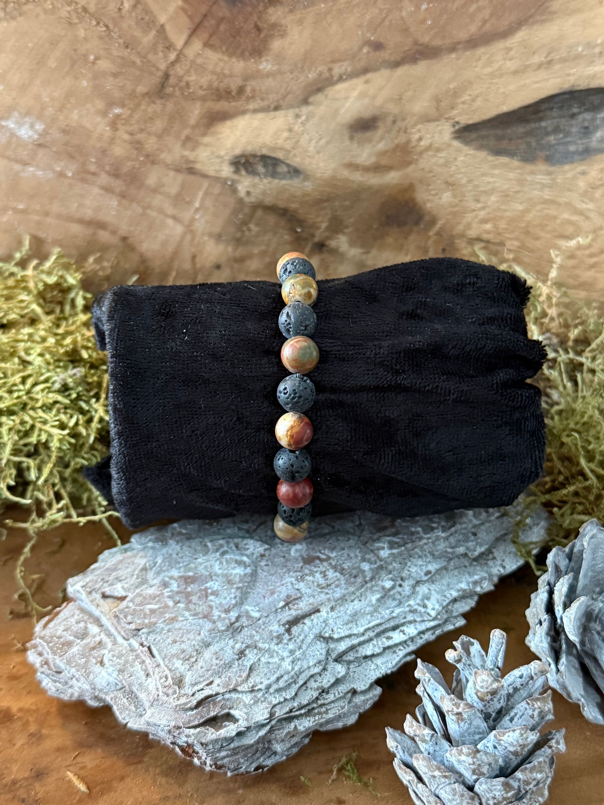 Armband gemaakt van bruine, rode en zwarte kralen op een zwarte stof, bevestigd op hout en mos.