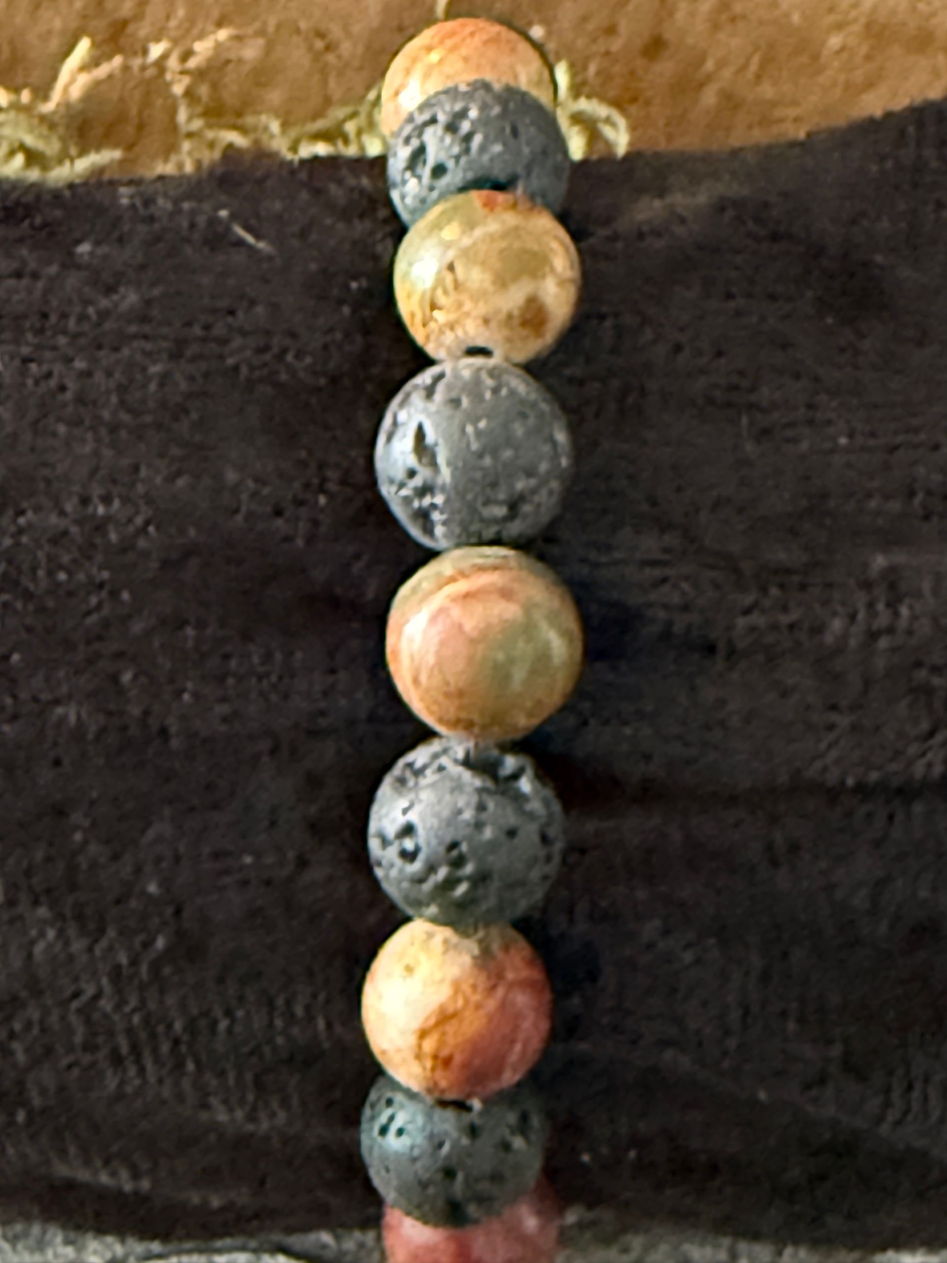 Armband gemaakt van bruine, rode en zwarte kralen op een zwarte stof, bevestigd op hout en mos.