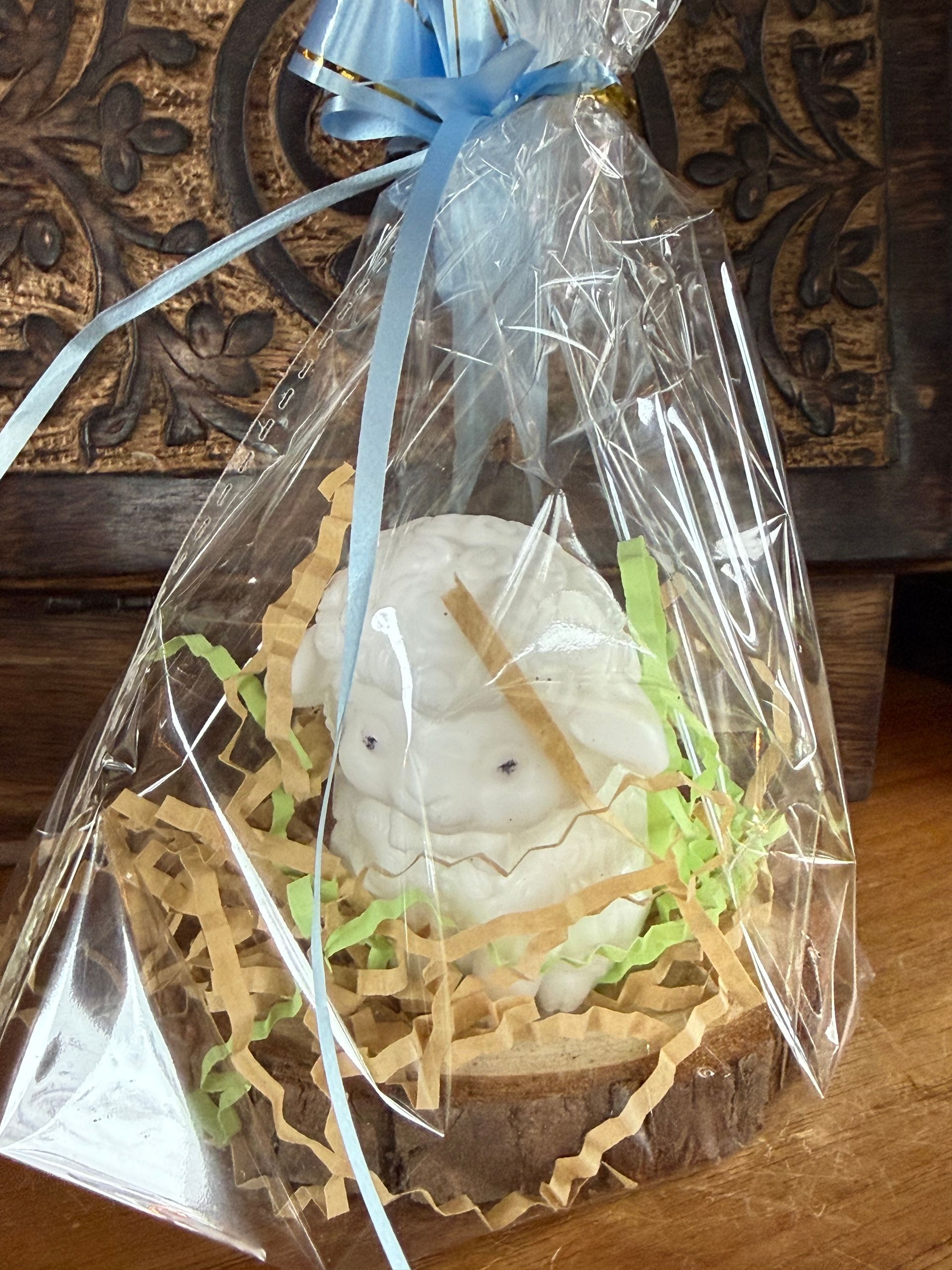 Een witte kaars in de vorm van een schaap staat op een houten plank, omringd door dennenappels en mos.