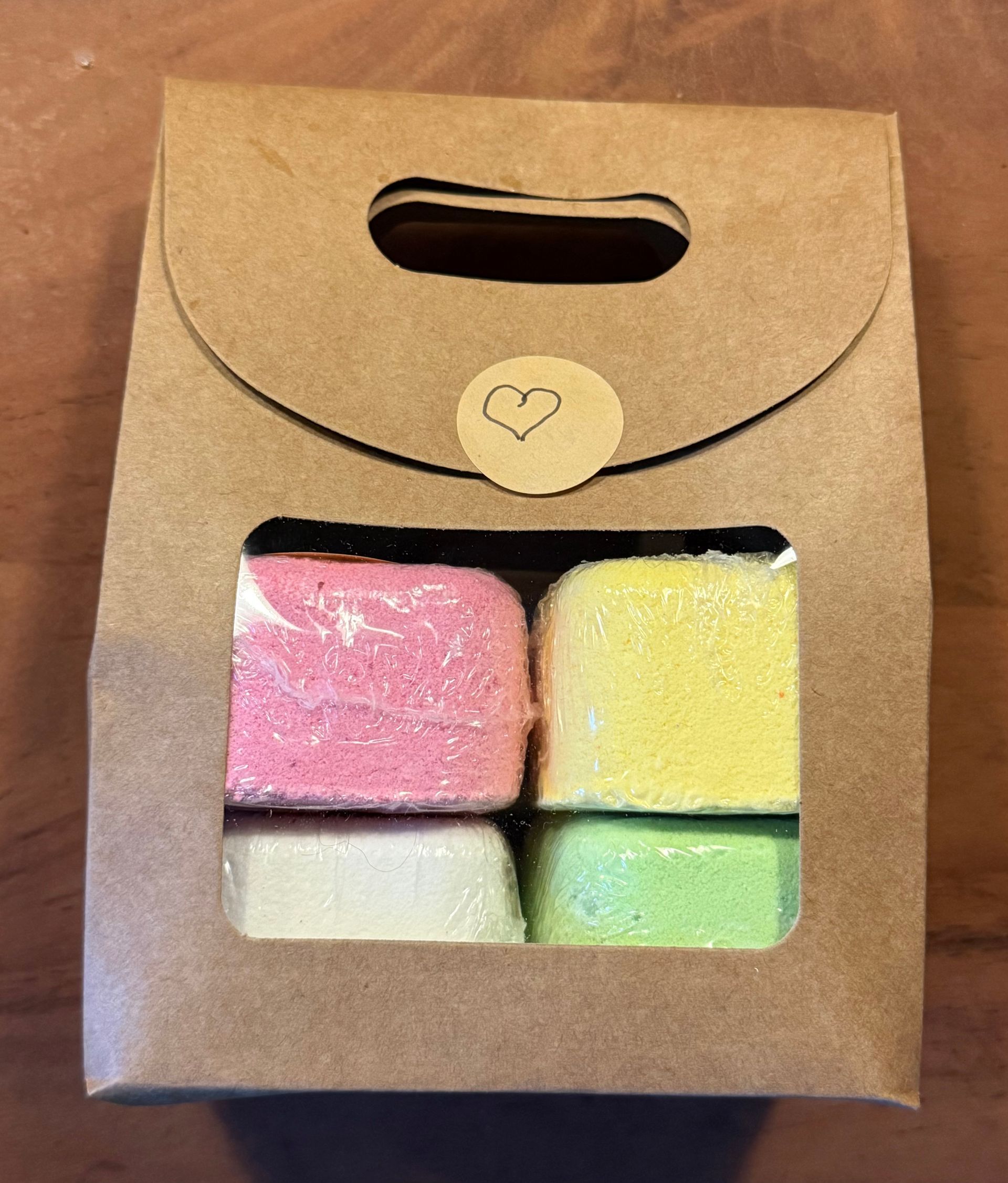 Cadeautasje met kleurrijke badbommen, waarvan er één op een houten zeepbakje ligt, met een wazige bokeh-achtergrond.