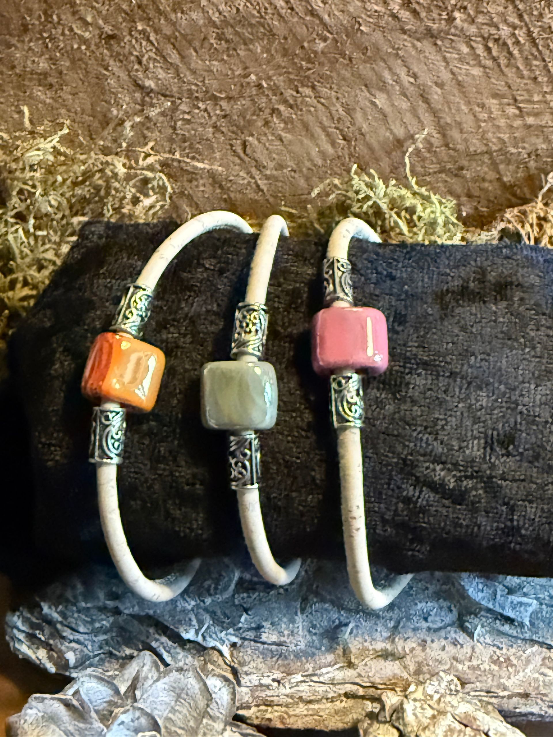 Drie kleurrijke kralenarmbanden op een zwarte display met een mosachtige achtergrond.