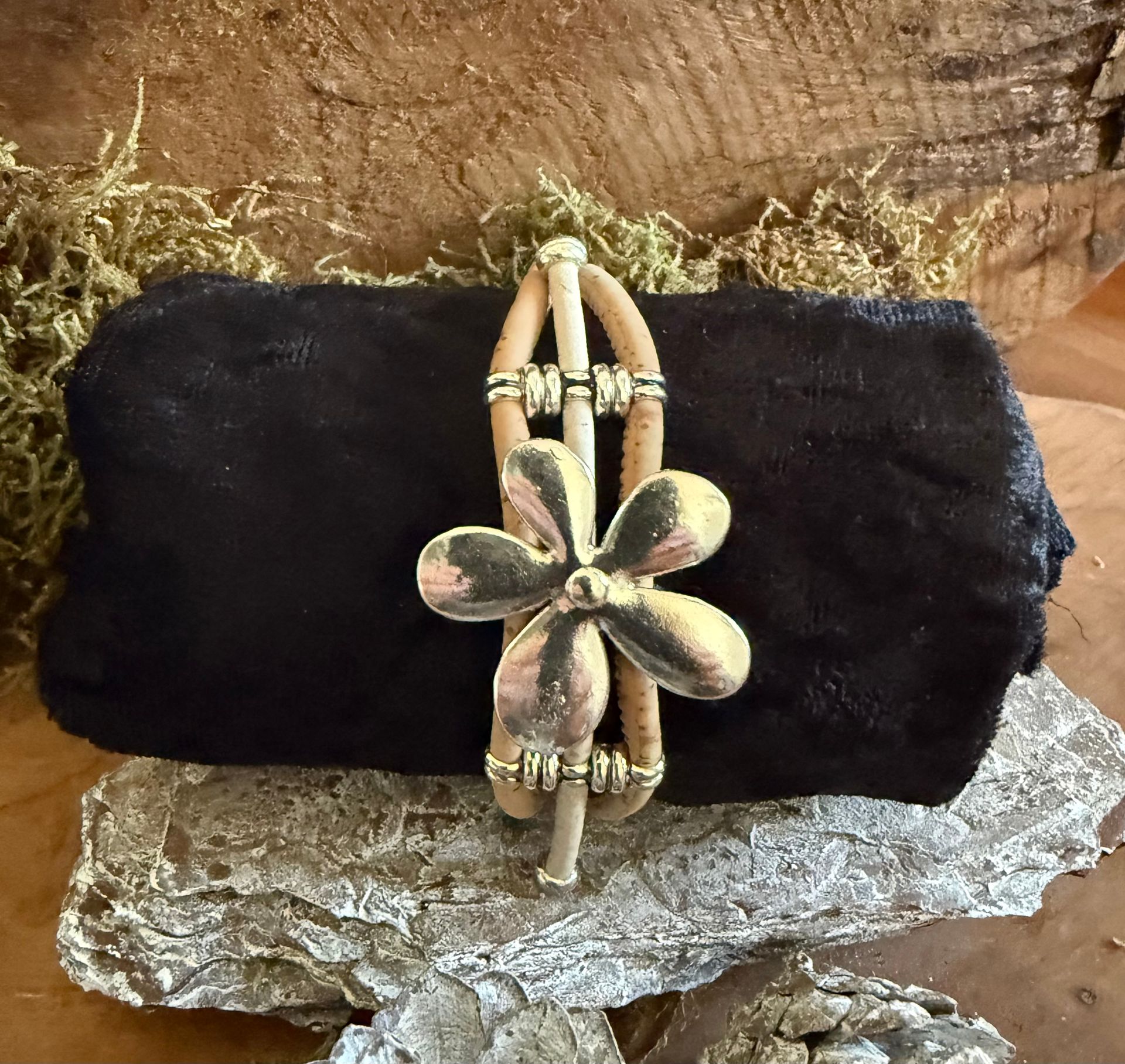 Drie bloemvormige armbanden met accenten liggen op een zwart kleed met zilveren dennenappels, op een houten ondergrond.