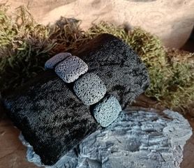 Zwart vulkanisch gesteente met kleinere grijze stenen erop, mos op de achtergrond.