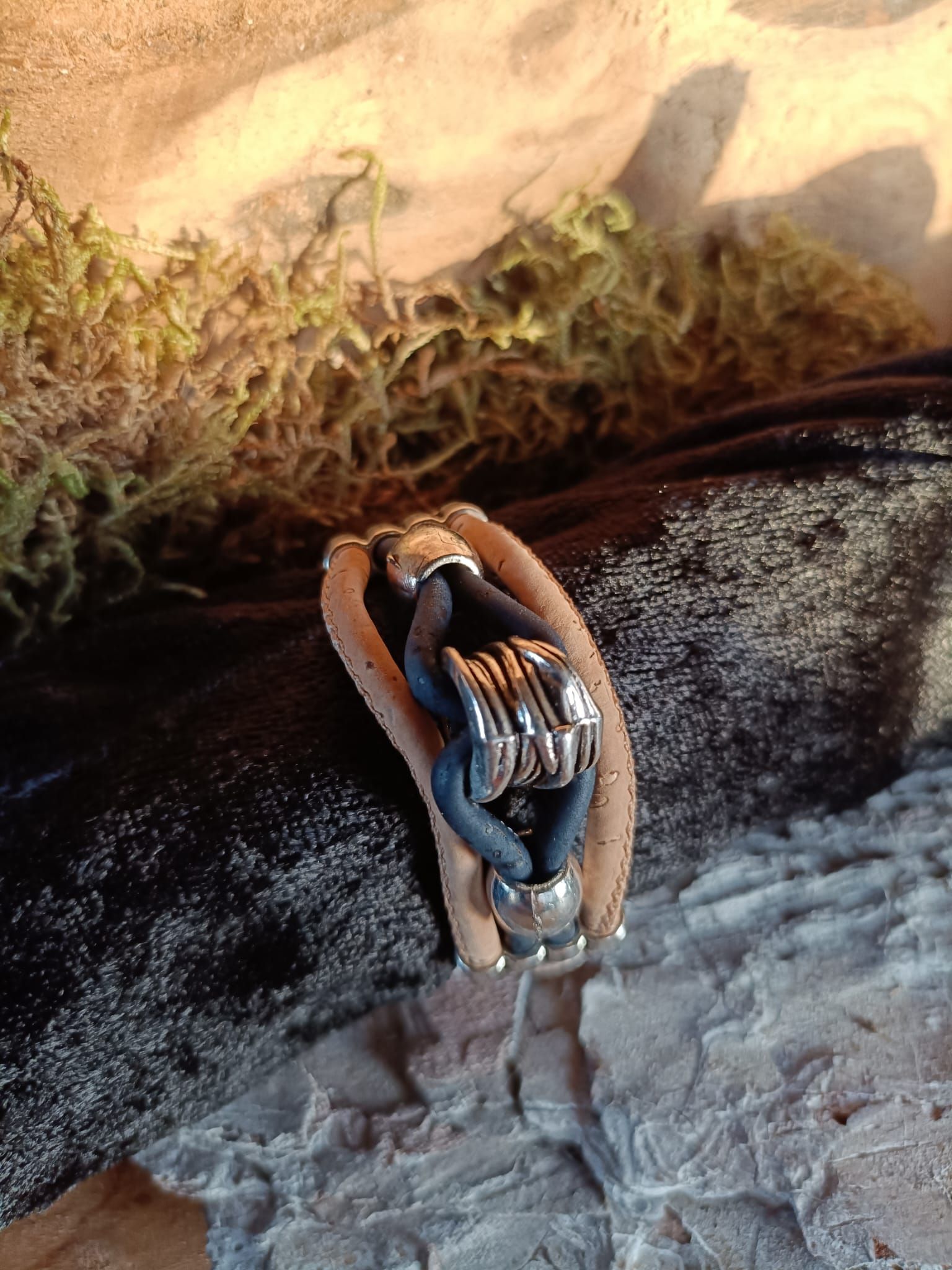 Armband met zilveren accenten en blauw koord, rustend op een gestructureerde ondergrond met mos.