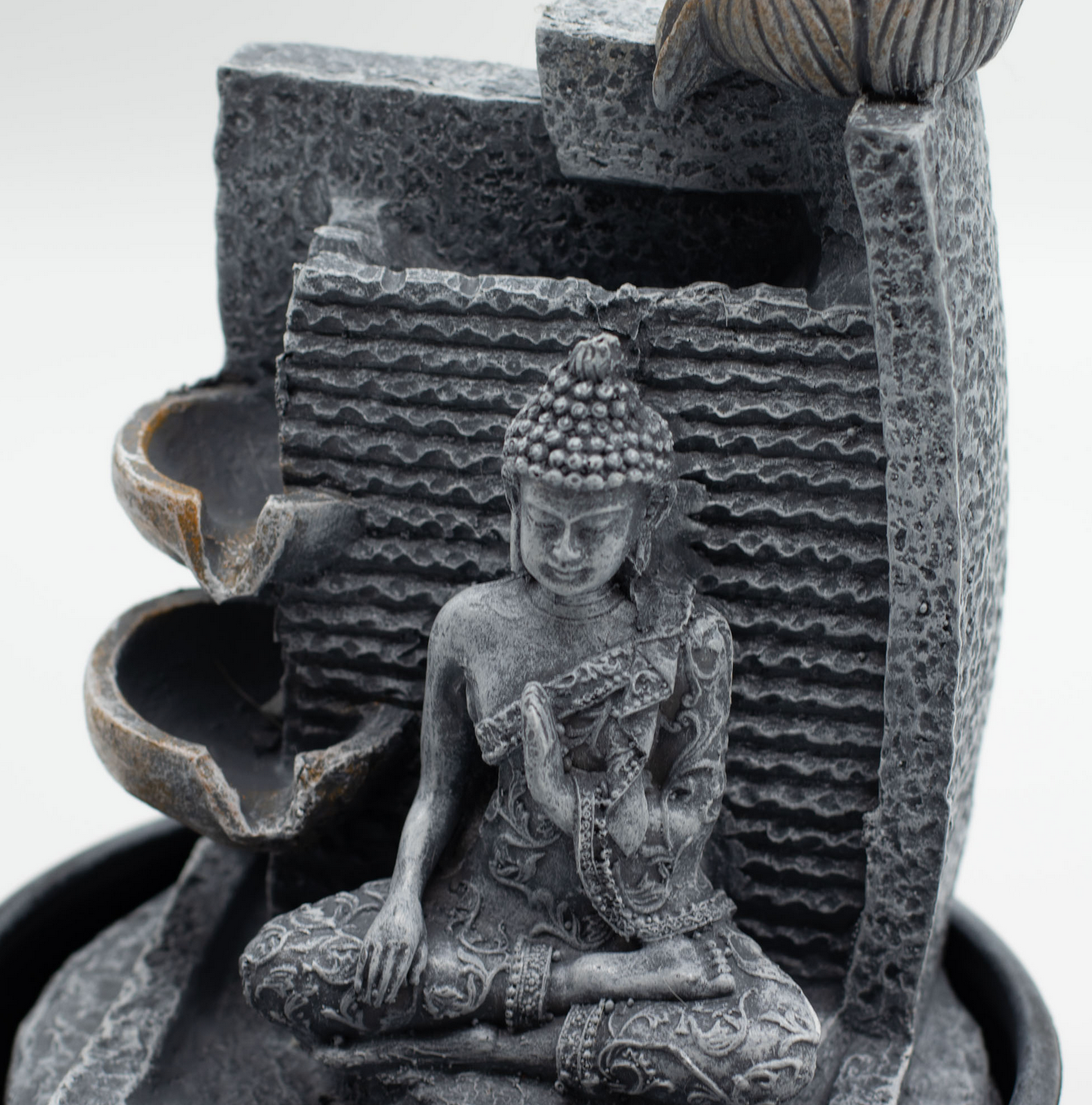 Een Boeddha-fontein voor op het bureau, donkergrijs, met water dat in trapsgewijze vorm in een kom stroomt.