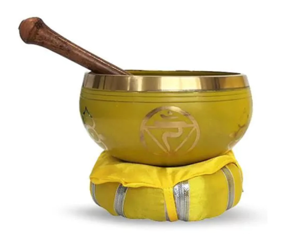 Gele klankschaal met houten hamer, geplaatst op een geel kussen, tegen een witte achtergrond.