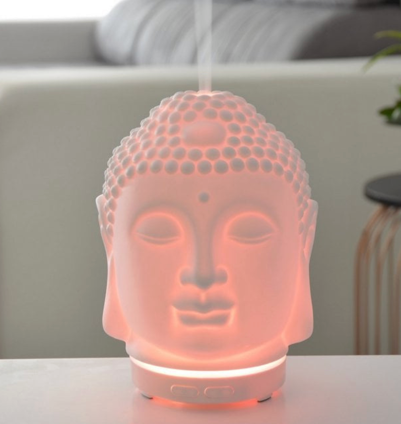 Witte olieverspreider in de vorm van een Boeddha-hoofd, die stoom afgeeft en zachtjes brandt.