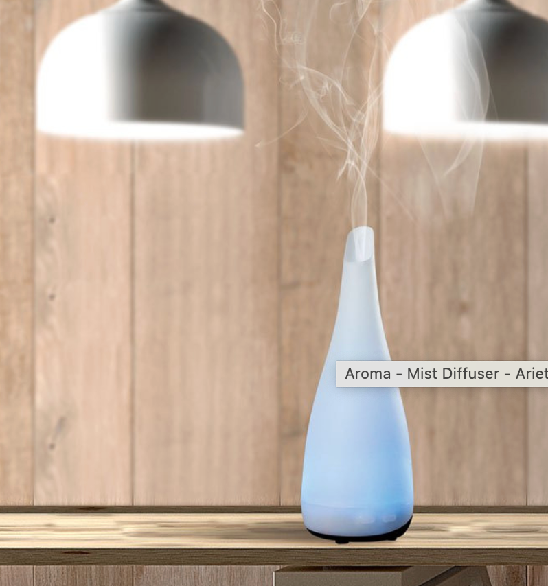 Witte aromadiffuser die nevel verspreidt, op een houten oppervlak met twee bovenliggende lampen.