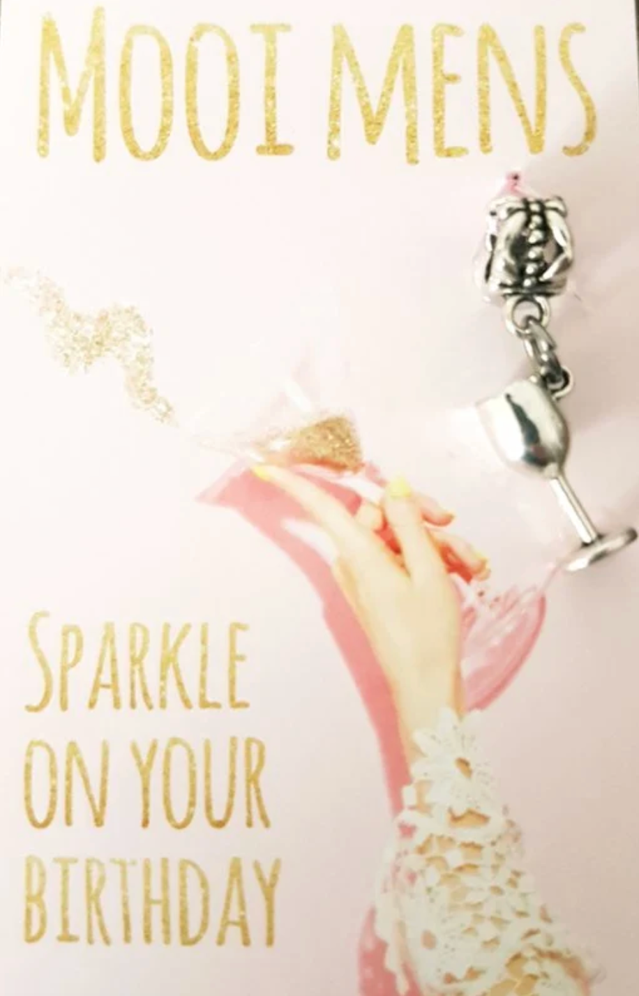 Roze verjaardagskaart met gouden tekst en een hand die een champagneglas vasthoudt; er is een bedeltje aan bevestigd.