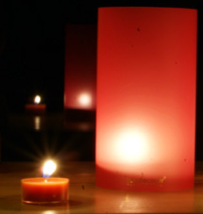 Kaarsvlammen verlichten een donkere kamer; één kleine, twee achter een grote rode cilinder.