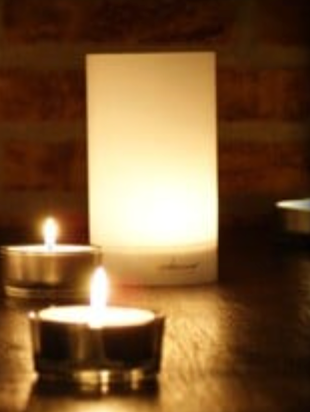 Witte, gloeiende lantaarn met twee brandende theelichtjes op een donkere tafel, met een bakstenen achtergrond.