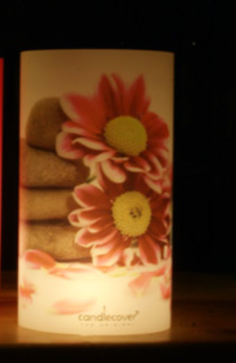 Cilindervormige kaars met roze madeliefjes en gestapelde steentjes; stralend van het licht. 