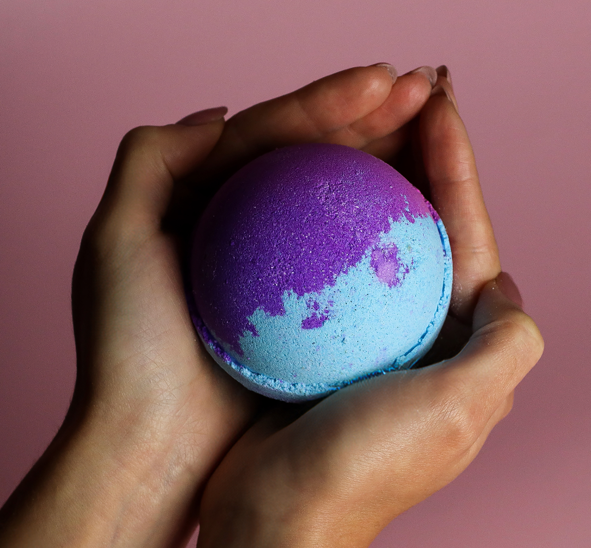 Een ronde bruisbal, half blauw en half paars, ligt op een bruine ondergrond.