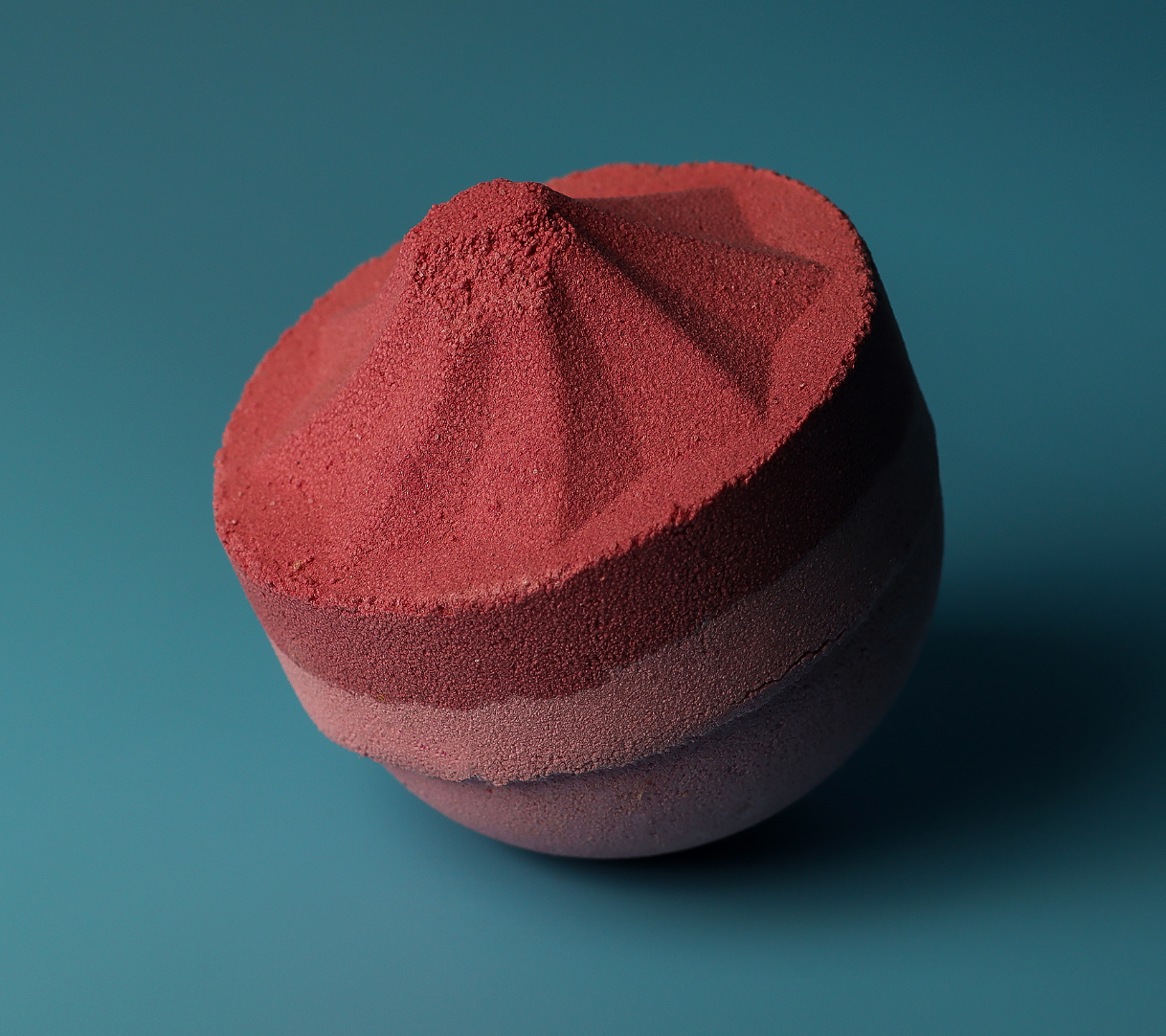 Rode, gelaagde bruisbal op een turquoise achtergrond; het bovenste gedeelte heeft de vorm van een berg.