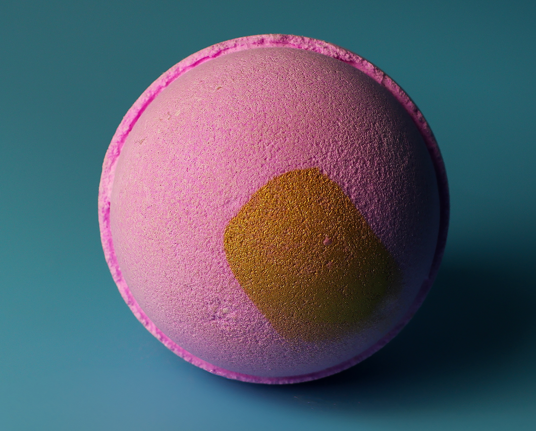 Roze bruisbal voor in bad met gouden glitterdetails op een blauwe achtergrond.