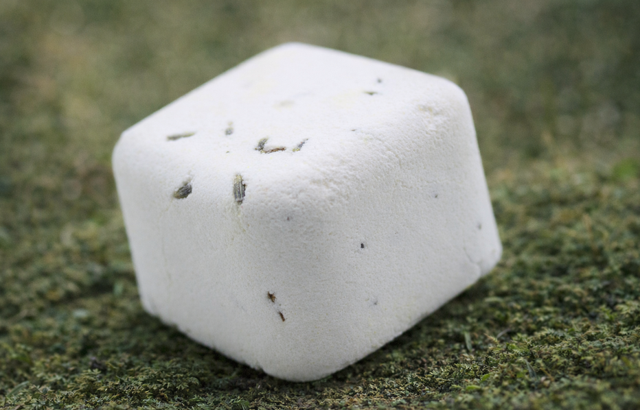 Witte, kubusvormige bruisbal met donkere spikkels, op een bedje van groen mos.