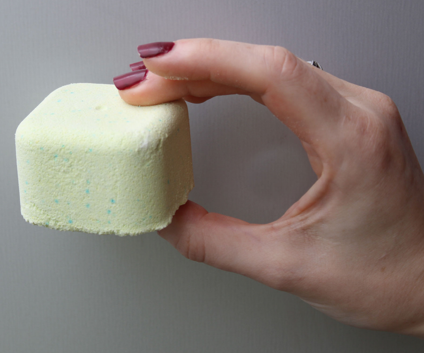 Vierkant groen schoendeodorant op een grijze handdoek, met hardloopschoenen en citrusvruchten op de achtergrond.