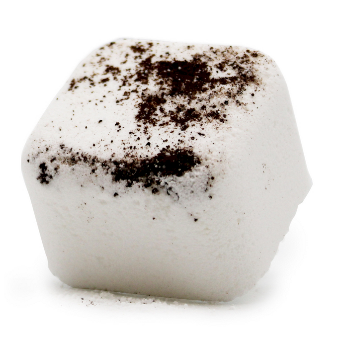 Witte bruisbal voor in bad met bruin poeder, omringd door muntblaadjes, citroenschijfjes en gember.