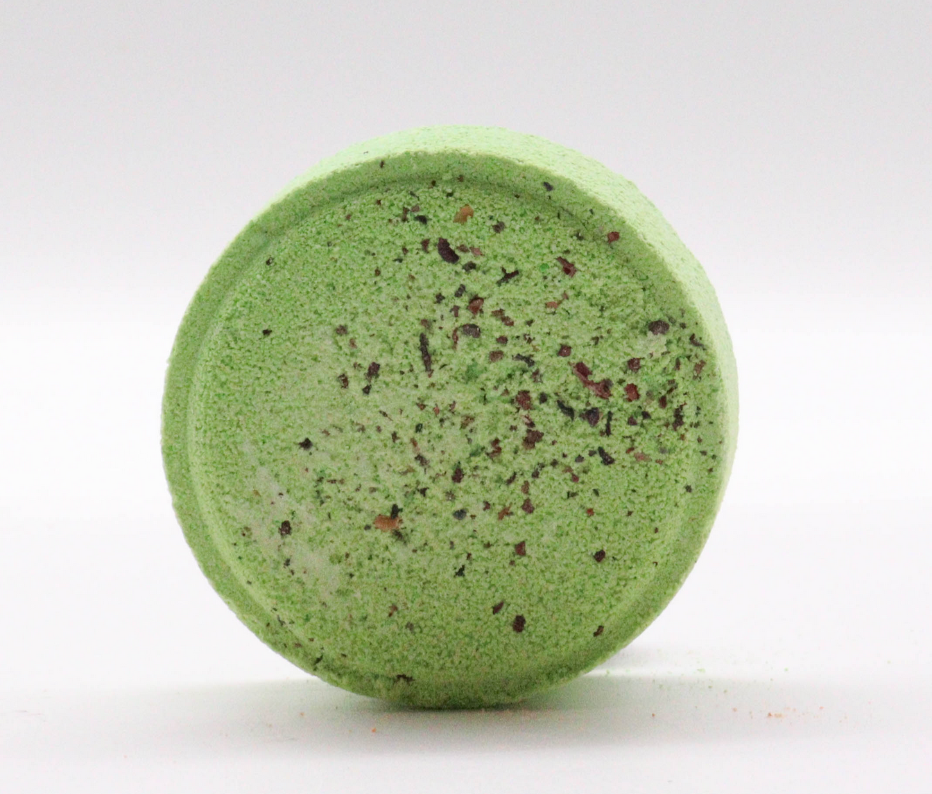 Groene bruisbal voor in bad, omringd door kruiden, fruit en handdoeken op een lichte ondergrond.