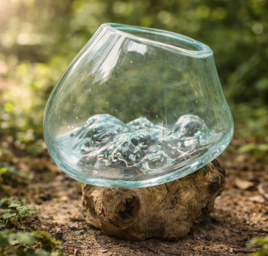 Glazen terrarium  gebeeldhouwd interieur, geplaatst op een verweerde houten sokkel buiten te midden van groen.