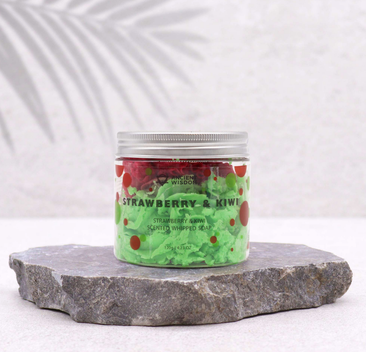 Potje luchtige zeep met aardbei- en kiwigeur, in rode en groene laagjes. Omringd door schijfjes aardbei en kiwi.