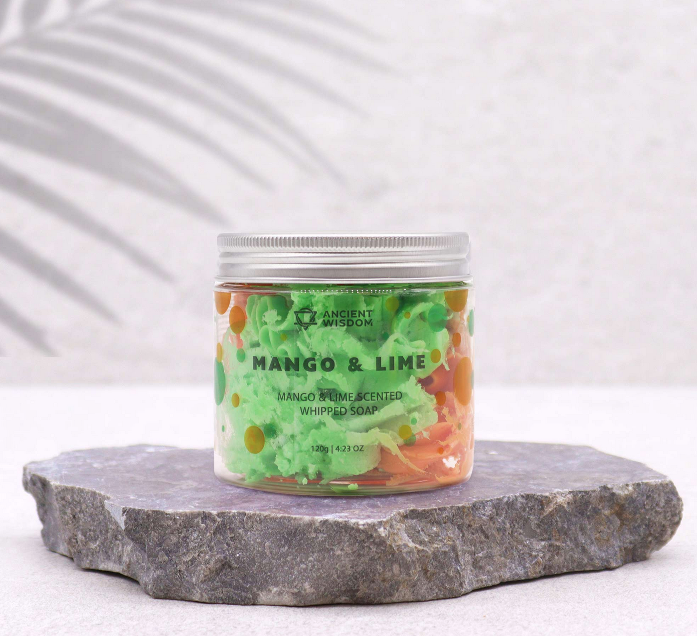 Potje zeep met mango- en limoensmaak, groen en oranje, met fruit op de achtergrond.