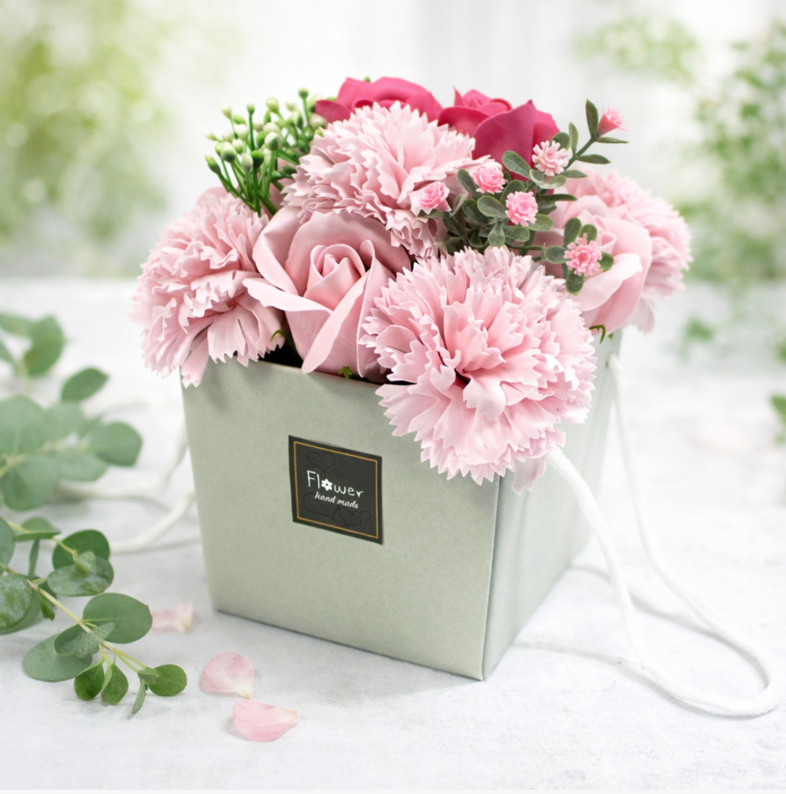 Een boeket roze anjers en rozen in een vierkante geschenkdoos met het opschrift 