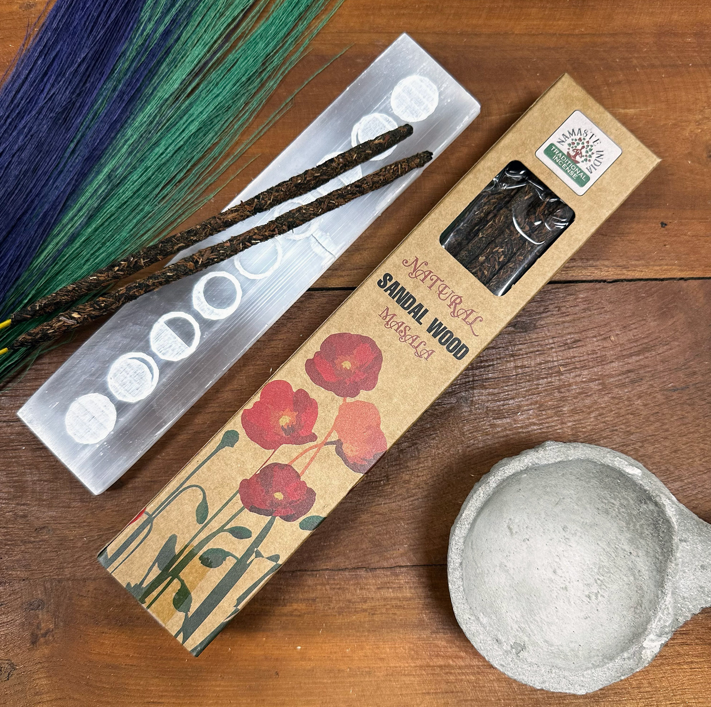 Wierookstokjes, een seleniethouder en een vijzel op een houten ondergrond. Bruine verpakking met rode bloemen.
